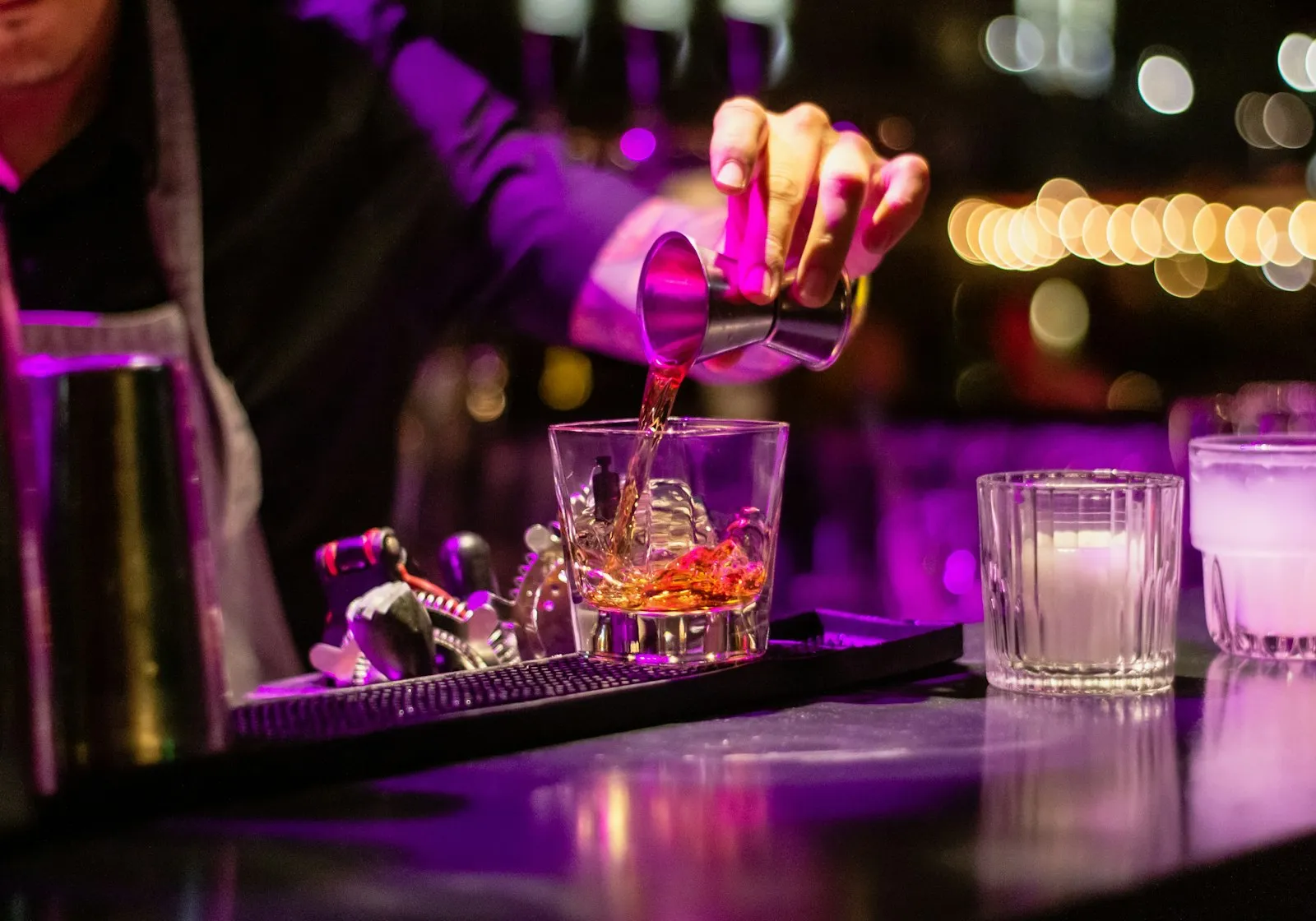 Bartender che versa un distillato in un bicchiere al banco bar